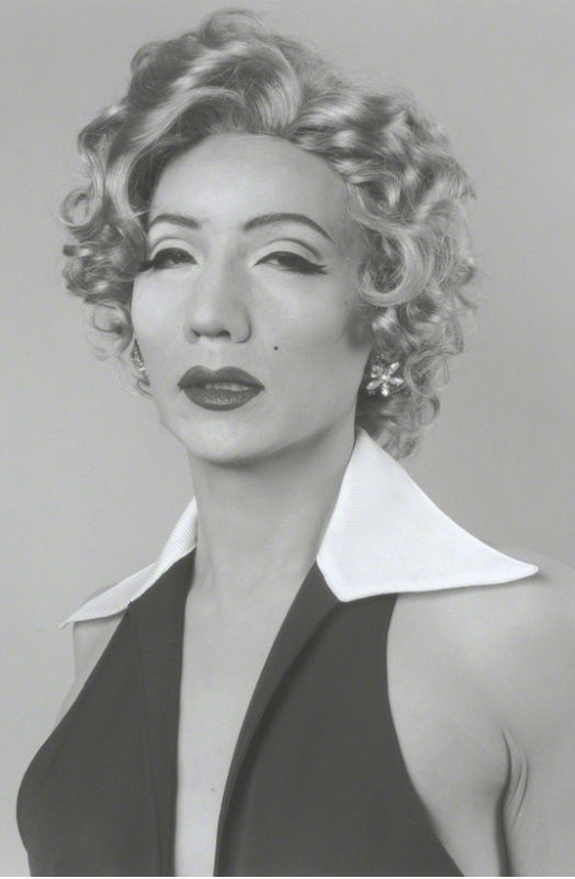 A woman wearing a short curly light-colored wig, dark eyeliner and a false beauty mark on her cheek in an emulation of Marilyn Monroe's iconic look.