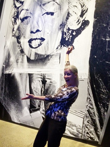A person gestures with wide open arms at a large print of Marilyn Monroe.