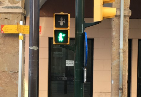 A close view of a pedestrian crossing signal using folkloric creatures as the pedestrians. The lower section of the signal is lit and emits green light.