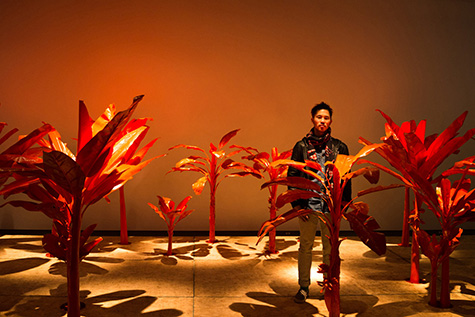 A man painted the color orange walking through a grove of green banana trees.