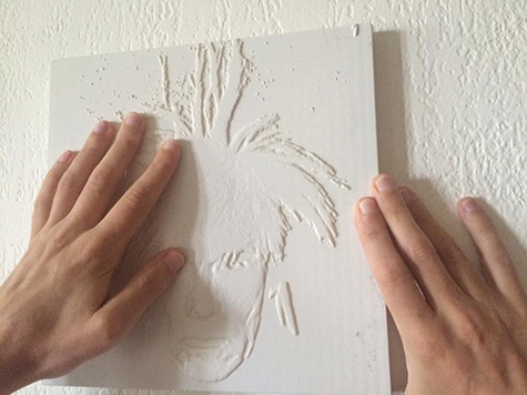 Two hands holding a 12 by 12 inch white 3D-printed reproduction of a man's face and wig, a reproduction of Andy Warhol's 1986 Self-Portrait.