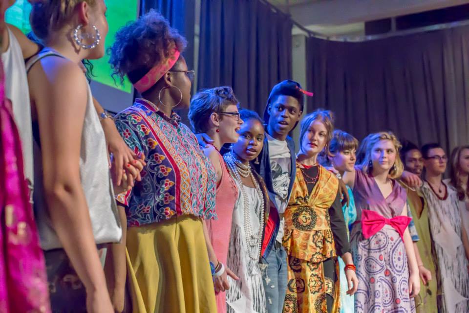 A row of teens participating in a fashion show. They are wearing bright, colorful garments.