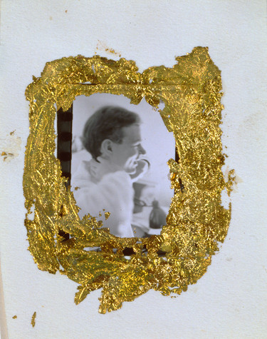 A photograph of Andy Warhol as a young man, shown here in profile. He faces the right side of the image, and the photograph has been affixed to a plain white piece of paper using a thick ring of gold leaf.