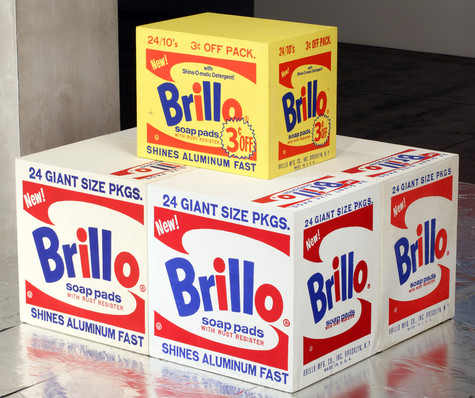 Four white boxes with the red and blue Brillo soap pads logo on them sit on a silver floor. On top of them is a smaller, yellow box with the same design and a sticker boasting that it is 3 cents off.