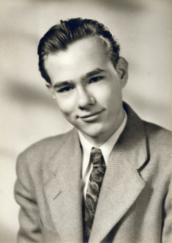 A photograph of Andy Warhol as a young man. His hair is combed back on his head and he smiles with closed lips, wearing a suit jacket and printed tie.