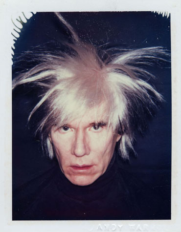 Andy Warhol, wearing a black turtleneck and with hair extremely disheveled looks at the viewer with an intense expression.