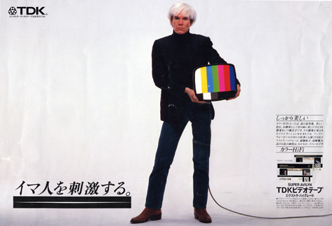 Andy Warhol stands facing front balancing a small television against his hip in a Japanese ad.