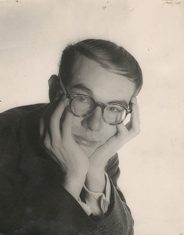 Andy Warhol as a young man sits with his chin in his hands.