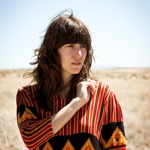 Singer-songwriter Eleanor Friedberger standing in a field of dry grass on a clear sunny day.