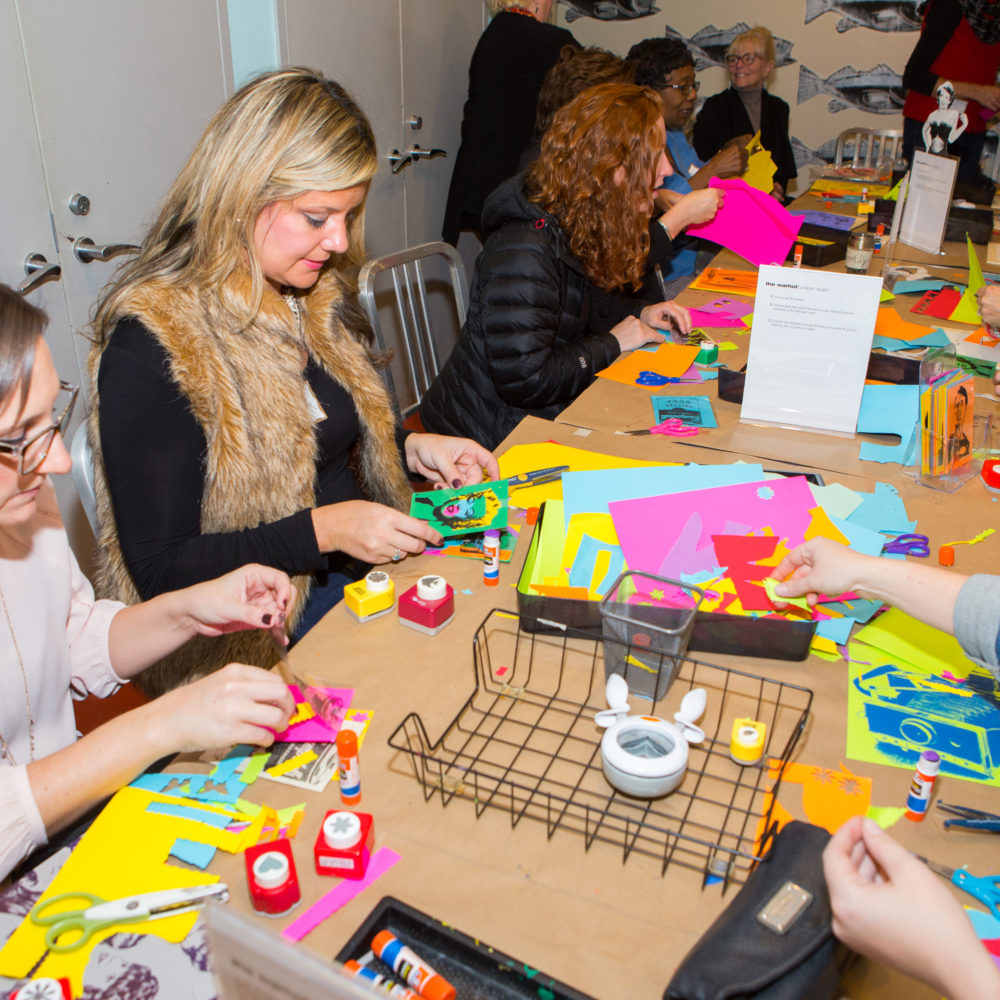 Educators sit around a long table during Teacher Open House 2016 as they create projects using colorful paper.