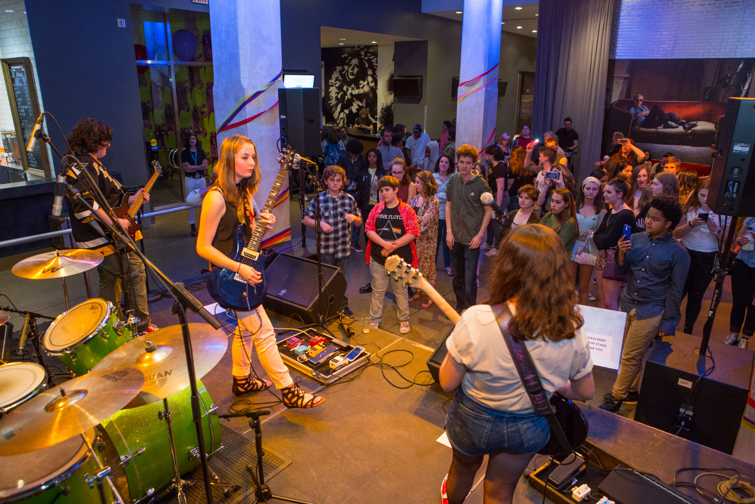 A teen band is playing on stage in front of an audience of mostly teens in The Warhol entrance space.