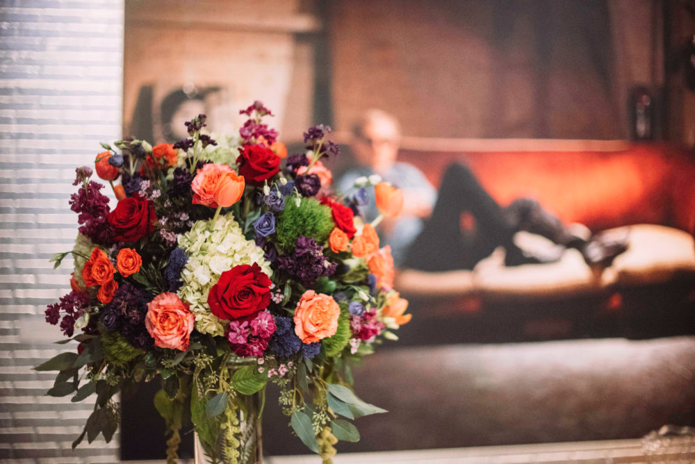 Flower centerpiece in front of a photograph of Warhol lounging on a red couch in the background.