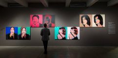 A person standing in a museum gallery views four pairs of large Warhol screen prints.