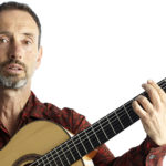 Musician Jonathan Richman plays a chord on an acoustic guitar.