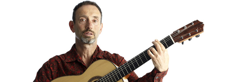 Musician Jonathan Richman plays a chord on an acoustic guitar.