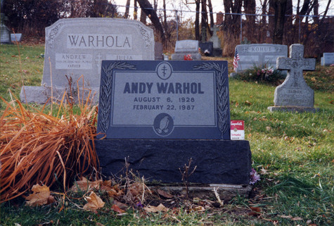 Photograph of Andy Warhol's headstone in autumn. In the background, other headstones, including a large headstone with the name Warhola across the top, can be seen.