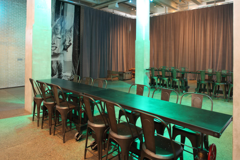 A photograph of the Andy Warhol Museum entrance Green light shines down on long metal tables surrounded by chairs.