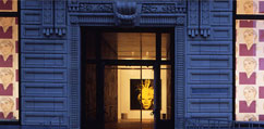 A view of the front facade of the Warhol Museum through which a large print of Andy Warhol can be seen.