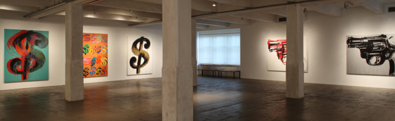View of the inside of the Warhol museum showing Warhol's dollar sign prints on one wall and pistol screen prints on the other.