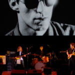 Four musicians playing on stage in front of a very large black and white image of a person wearing sunglasses.