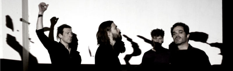 Members of the Chicago-based band Disappears pose in front of a large white wall.