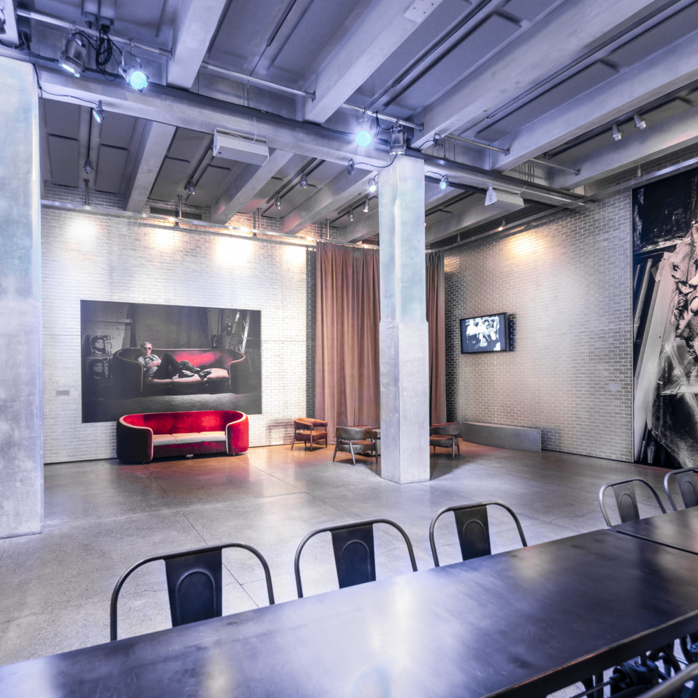 A photograph of the Andy Warhol museum entrance space. There is a long, silver table in the foreground and a red velvet couch pushed up against a far wall under a portrait of Andy Warhol reclining on a red velvet couch.