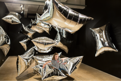 A girl plays in Andy Warhol's Silver Clouds installation. She is surrounded by floating silver pillow-shaped balloons.