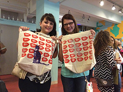 Two teachers hold up tote bags printed with Marilyn Monroe lips