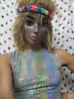 A woman in a shiny sequined top with a doll-like mask, short dirty blonde hair, and colorful sweatband
