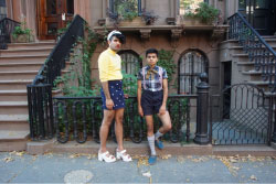 Two people stand in front of brownstone houses