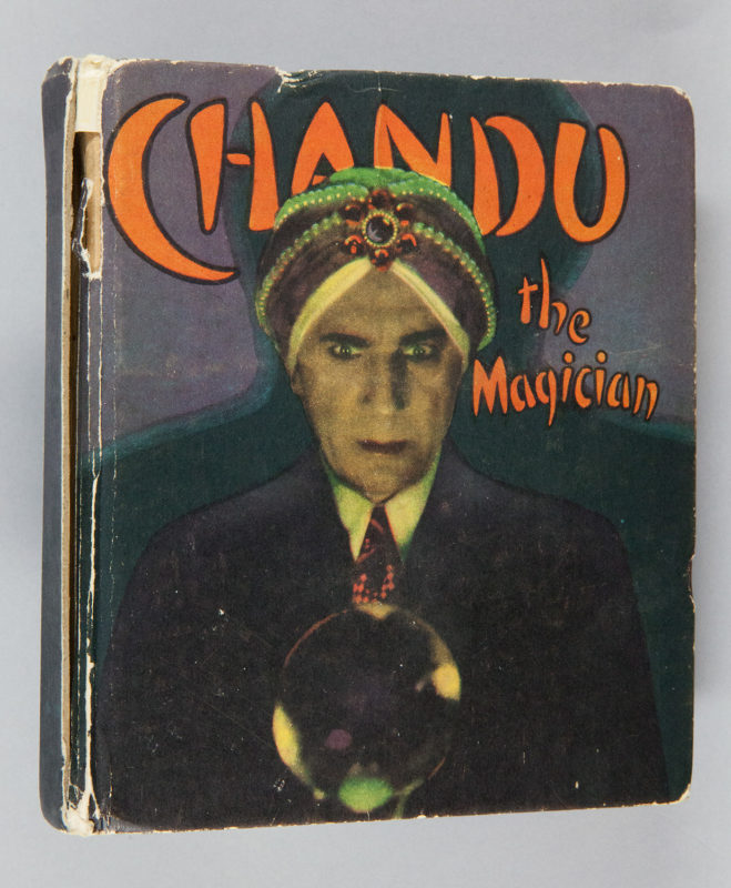 A photograph of an old book cover. A man in a suit and turban stands before a crystal ball, and the words “Chandu the magician” appear in the space around his head in orange text.