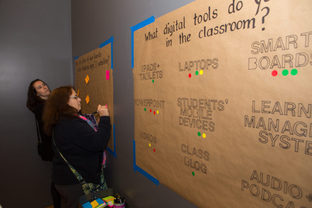 Teachers write their poll responses on sticky notes while standing in front of the Inspiration Wall
