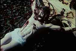 A still from the film A Fire In My Belly showing a painted sculpture of Christ on the cross.