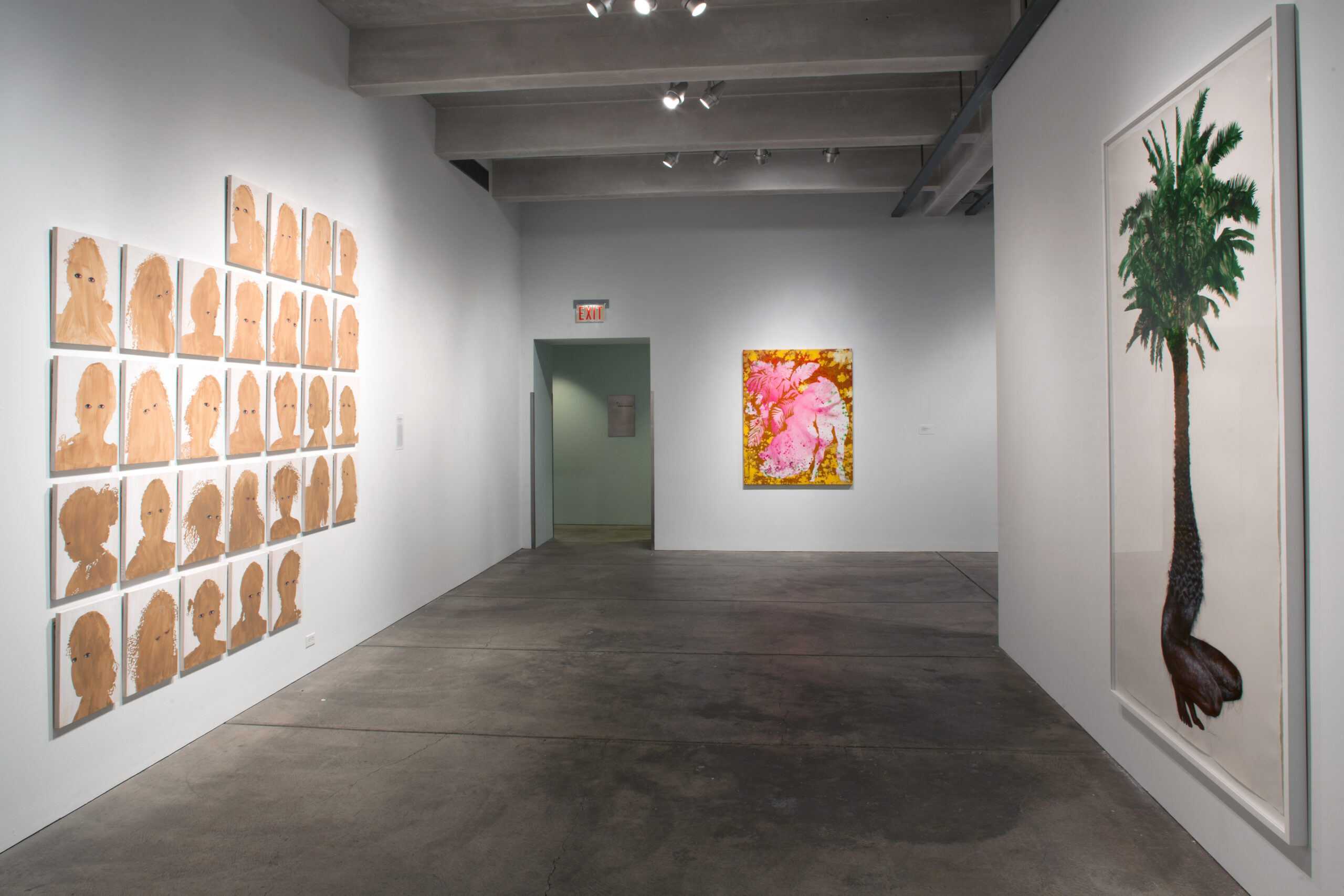 A photograph of Firelei Baez's Bloodlines exhibition. On the left wall is a series of sillhoutte portraits with eyes. On the right is a painting of a palm tree whose trunk ends in a pair of hairy legs. On the far wall is an abrastract painting in gold, pink, iand red.