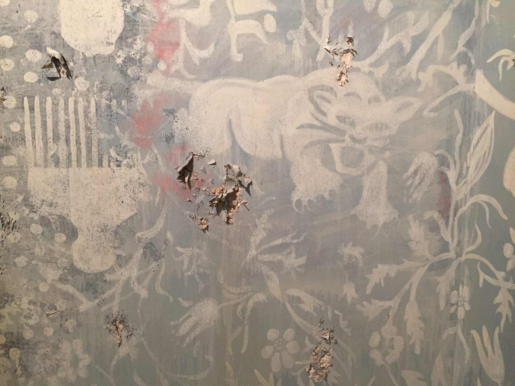 The wall of the Firelei Baez exhibition space, painted pale blue with white floral shapes. Paint has been scraped away in a few places on the wall.