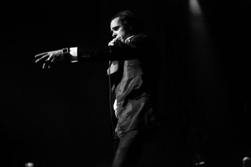 Black and white photograph of a man wearing a suit singing into a microphone.
