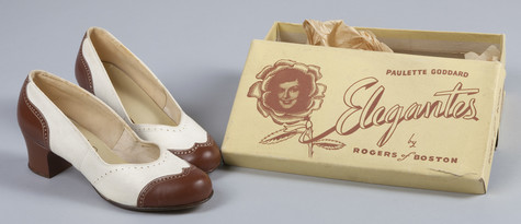 A photograph of white high-heeled shoes with brown wingtips sitting next to their box, which identifies them as Paulette Goodard’s Elegantes.