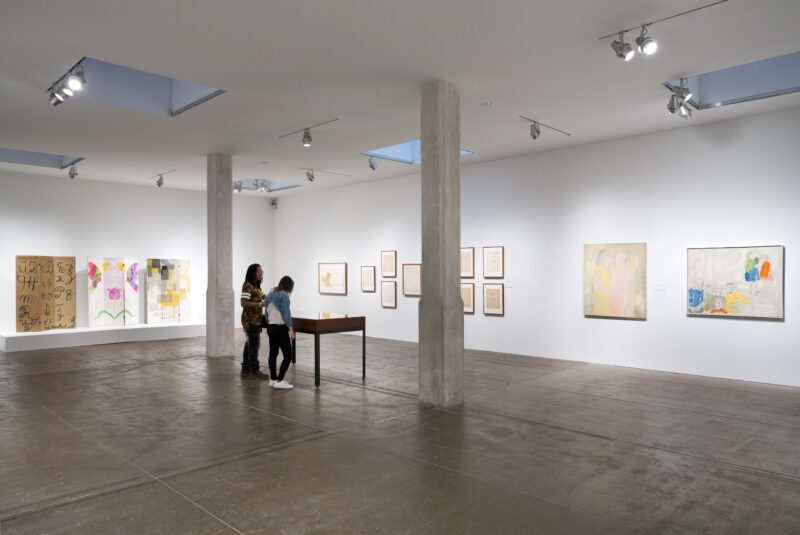 In a gallery of artworks by Andy Warhol, two people lean over a vitrine