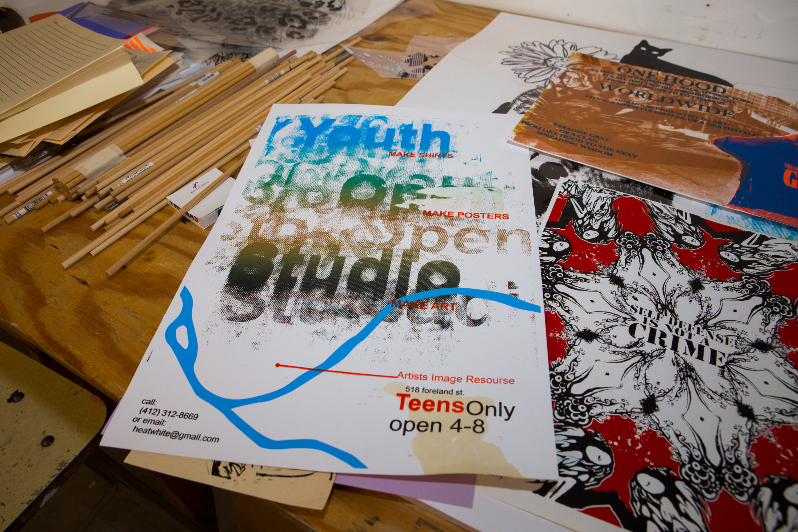 A poster of the Andy Warhol Museum's Youth Open Studio sits on a table with other posters and art supplies.