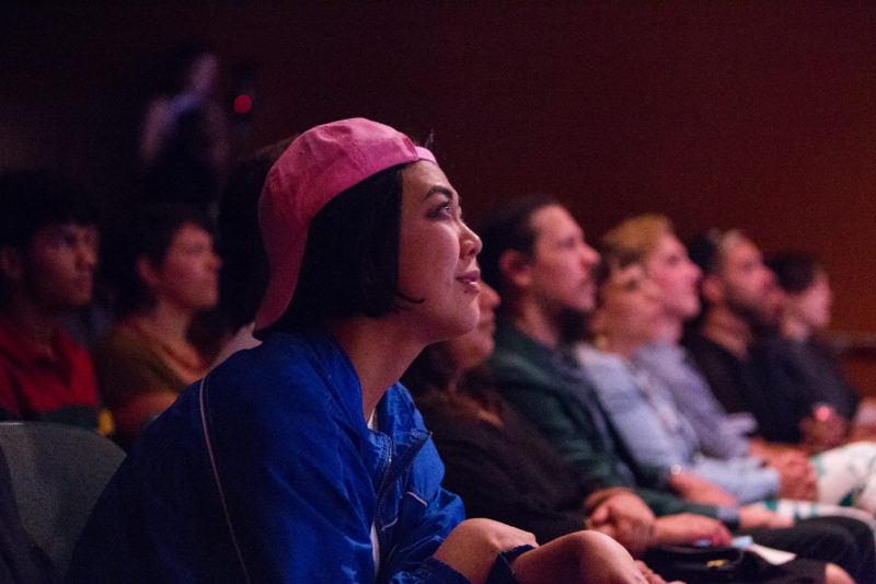 People are seated in an audience, rapt in attention to the performance happening to the right outside of the image's frame