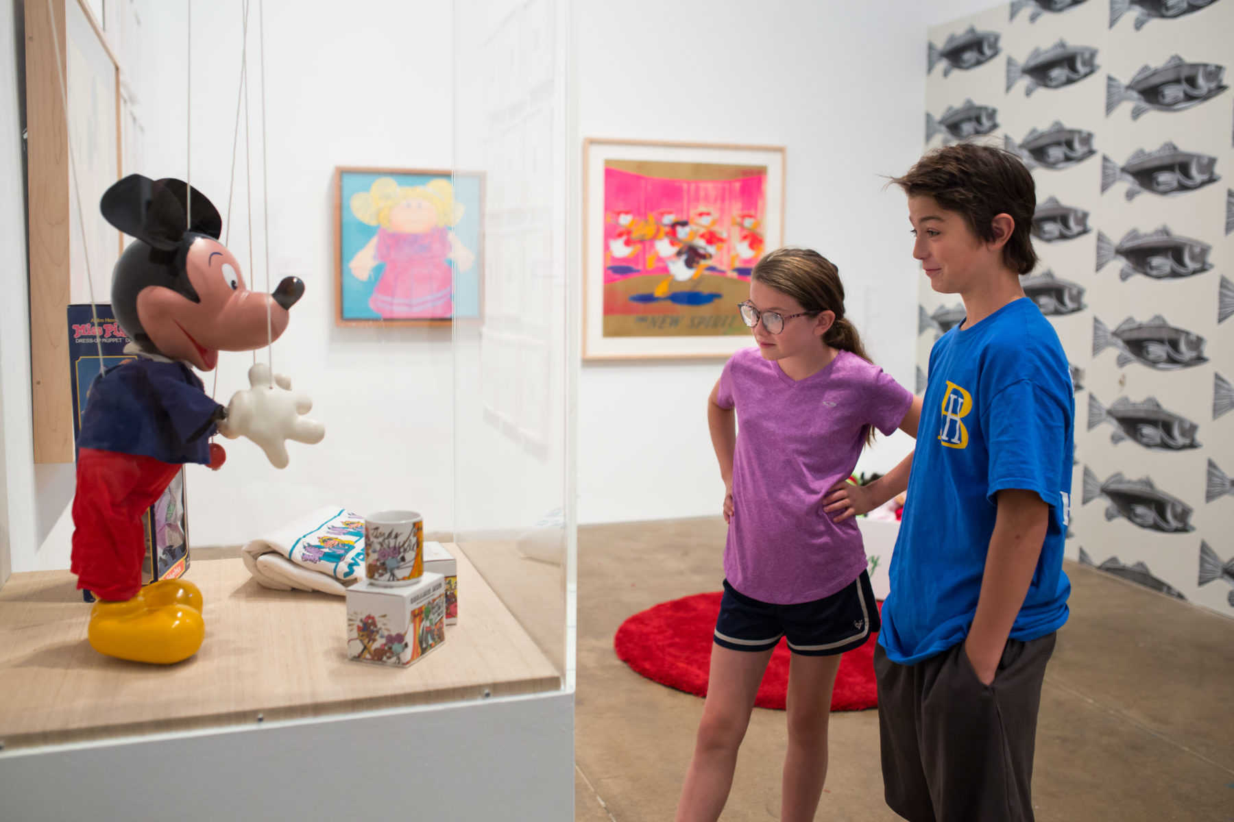 A boy in a blue t-shirt and a girl in a purple t-shirt with her hands on her hips look at a Micky Mouse display.