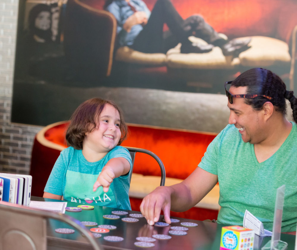 An adult and a young child laugh together while playing a table top game in the museum.