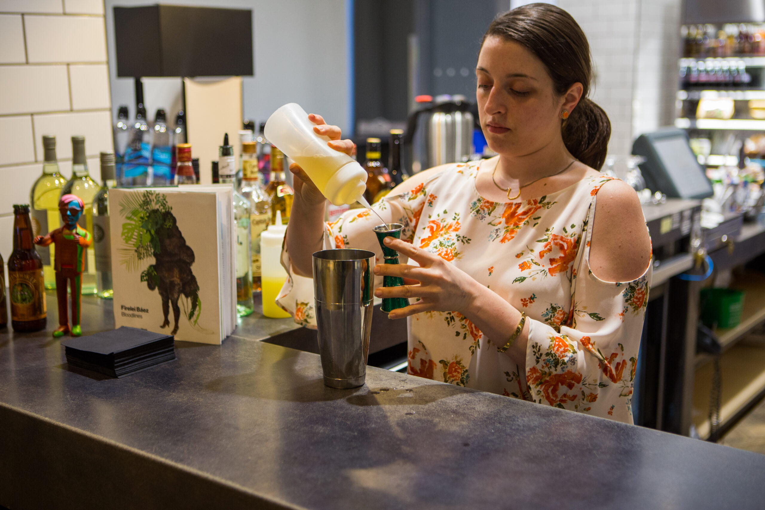 A woman in a floral print shirt mixes a drink at the Warhol Cafe during a Sip and Sketch event.
