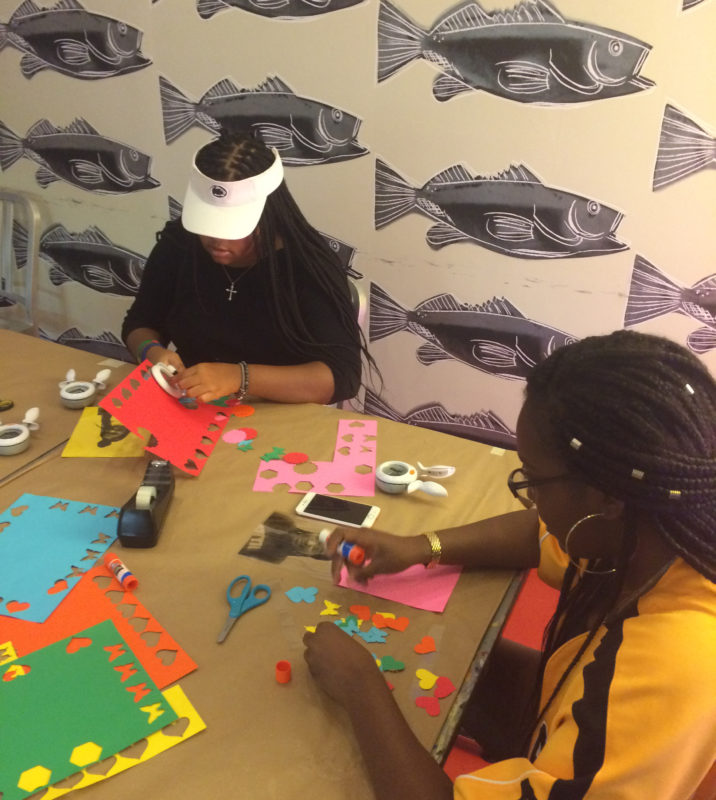 Two female students punch shapes such as butterflies, hearts, and octagons out of colorful pieces of construction paper in The Andy Warhol Museum’s Factory art studio.
