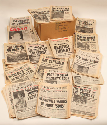 A photograph of one of Andy Warhol’s time capsules surrounded by its contents, dozens of copies of the New York Post with headlines that announce stories such as Millions Mourn Presley and Muslim Bands Terrorize D.C.
