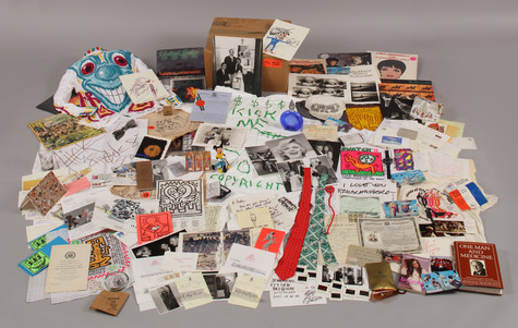 The contents of one of Warhol’s Time Capsules. There are several books, pieces of artwork by Keith Haring and Jean-Michel Basquiat, a hand painted turtleneck by Kenny Scharf with a large, blue cartoonish face painted on the front, a Mickey Mouse figurine, ties, postcards, and documents, among other things.