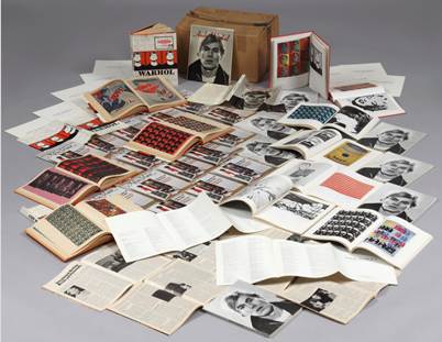 Books, articles, and photos of Andy Warhol artfully arranged with a cardboard box in the background.