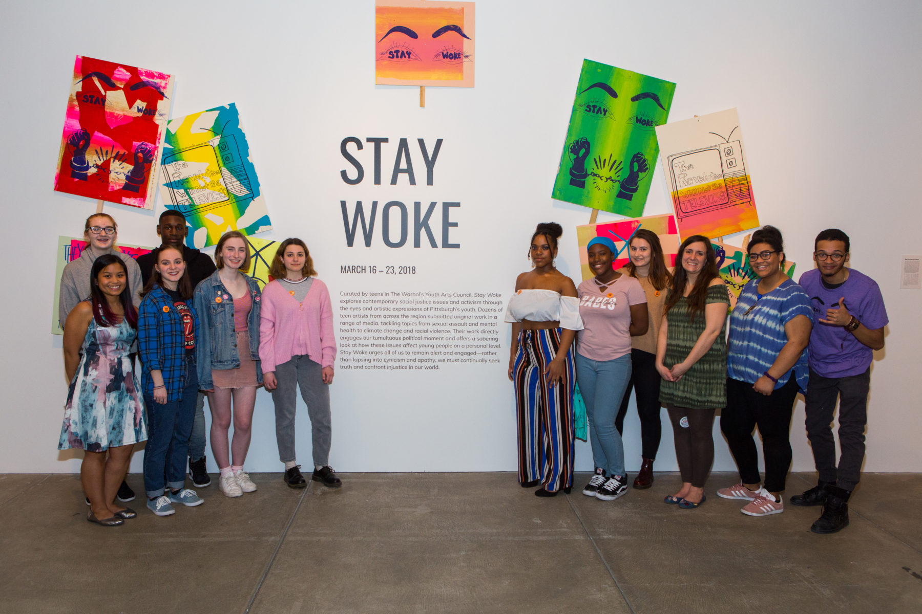 Group of students in front of colorful posters and large wall text that says Stay Woke