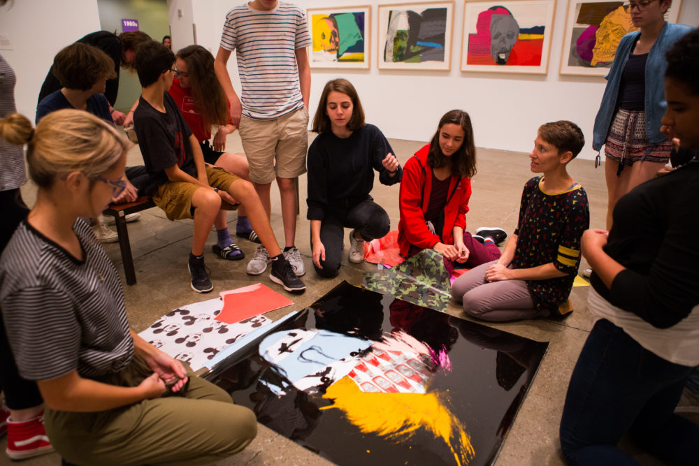 With prints of Warhol's Skulls in the background, teens sit in a circle and use pieces of acetate and patterned paper to create Warhol-inspired designs.
