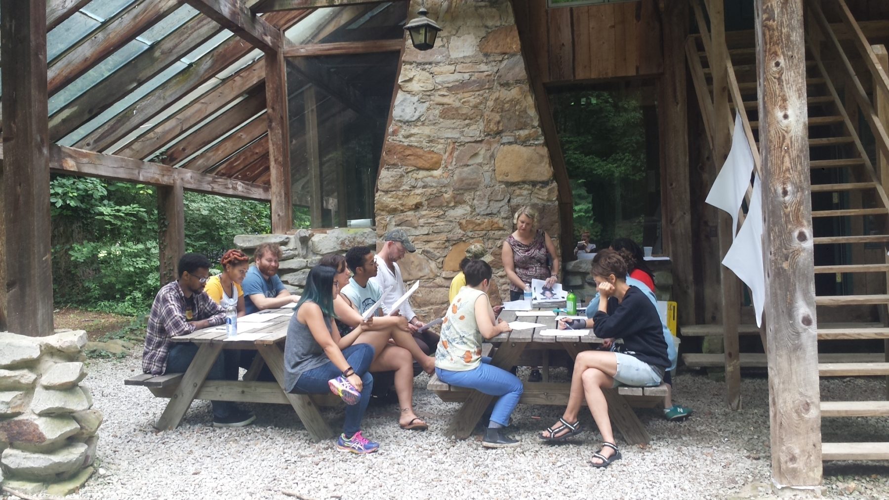 A group of staff members sits at picnic tables outside of a wooden and stone cabin.